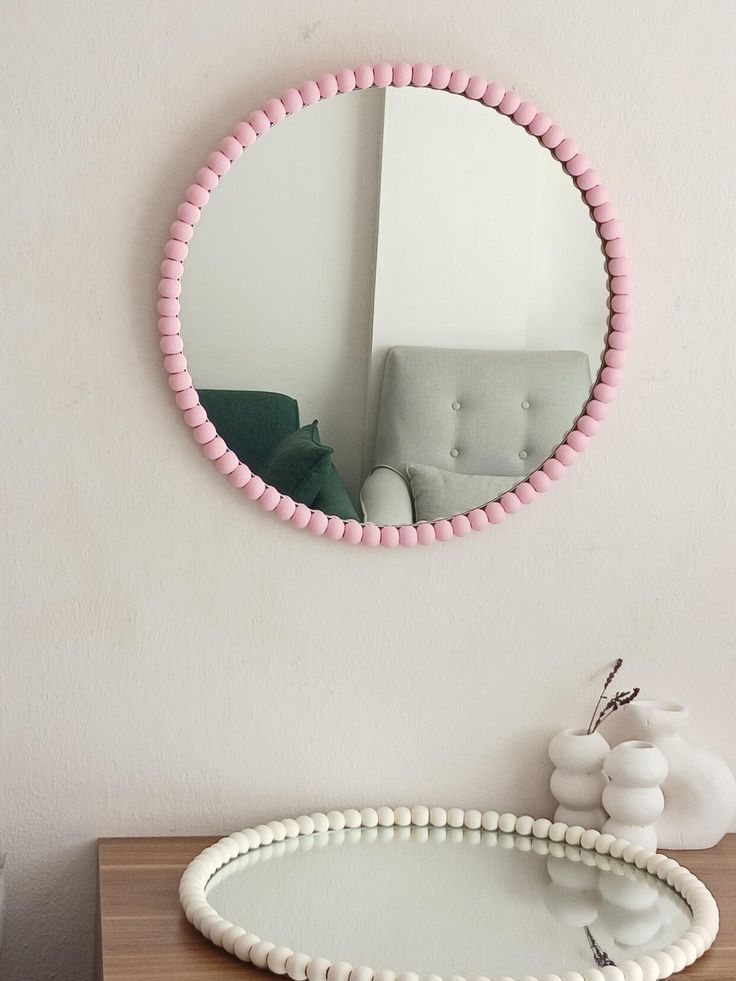 a round mirror sitting on top of a wooden table next to a white vase with flowers