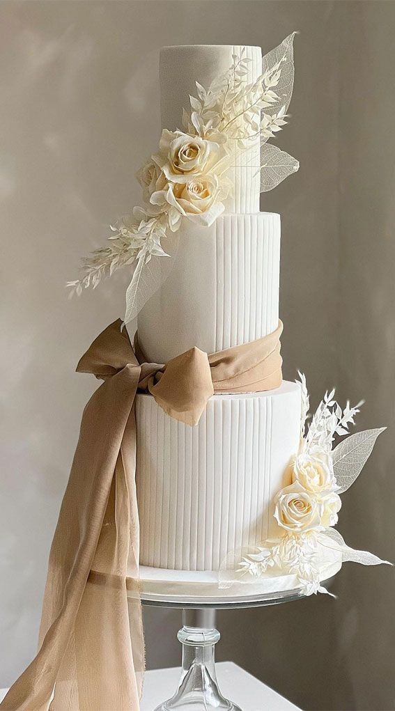 a three tiered wedding cake with flowers and ribbons on the top, sitting on a table