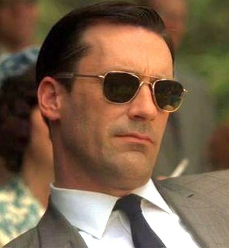 a man in a suit and sunglasses looking at something while people are standing behind him