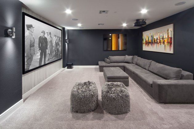 a large living room with grey couches and two ottomans on the floor, in front of a movie screen