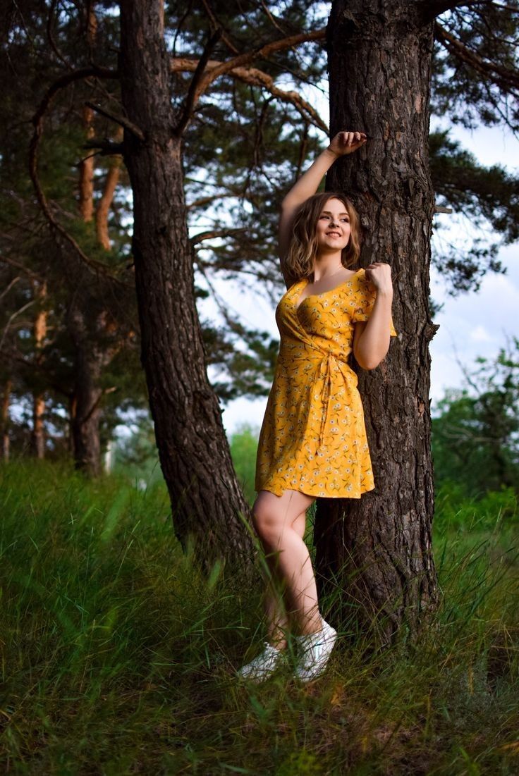 a woman in a yellow dress leaning against a tree