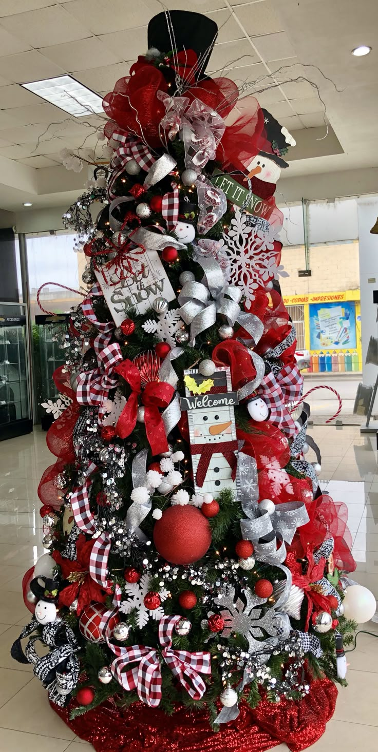 a christmas tree decorated with red, white and black ornaments in an airport lobby area