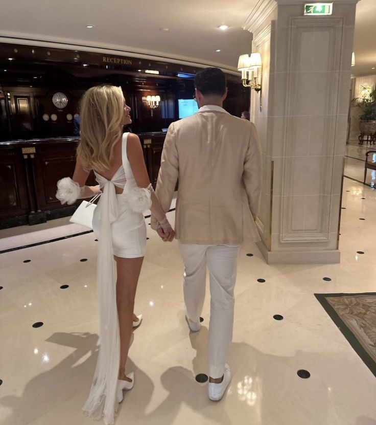 a man and woman walking through a hotel lobby holding each other's hands as they walk towards the reception area