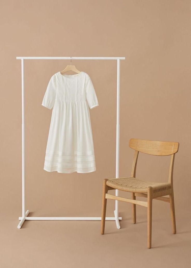 a white dress hanging on a clothes rack next to a wooden chair