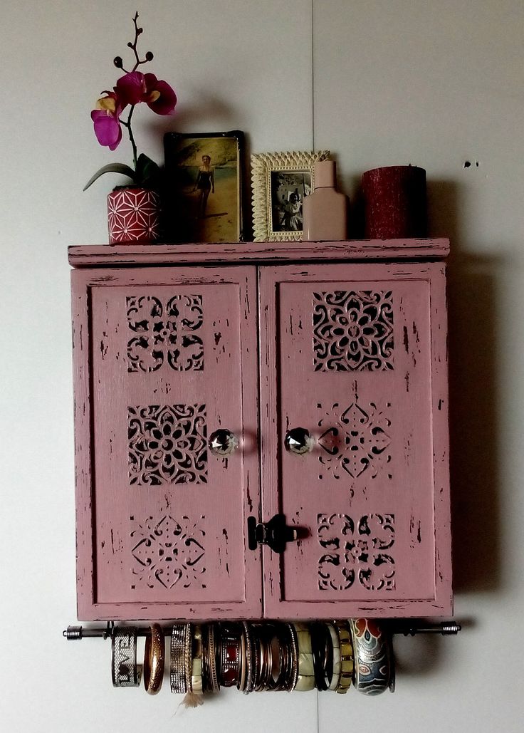 an old pink cabinet with rings on the door and flowers in vases next to it