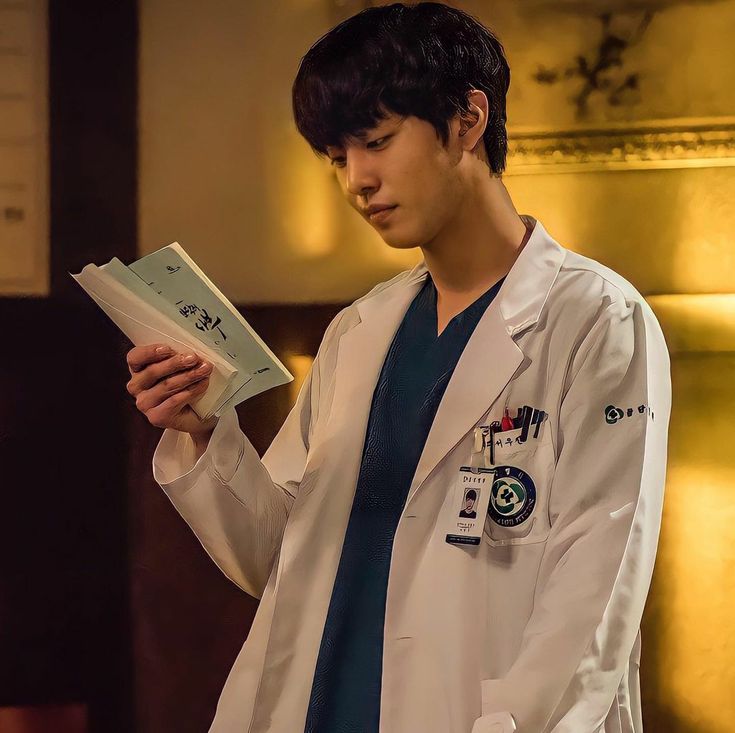 a male doctor in a white lab coat is holding a book and looking at it