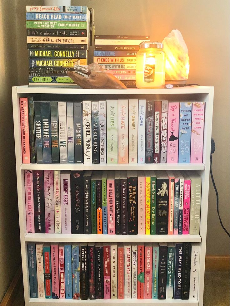 a bookshelf filled with lots of books next to a wall mounted light on top of it