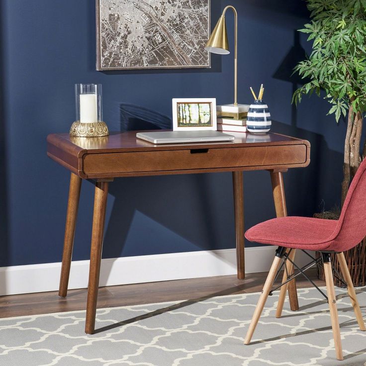 a desk with a red chair next to it and a painting on the wall behind it