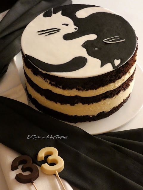 there is a cake decorated with black and white cats on the frosting, along with two chocolate pretzels