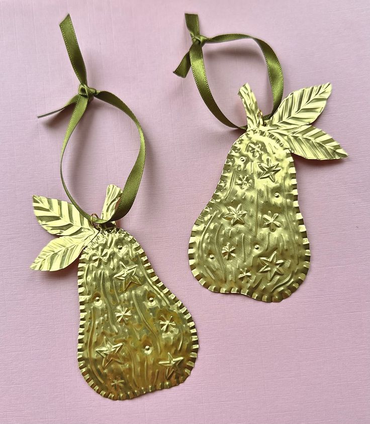 two metal pear ornaments with green ribbons on a pink tablecloth, one is gold and the other is silver