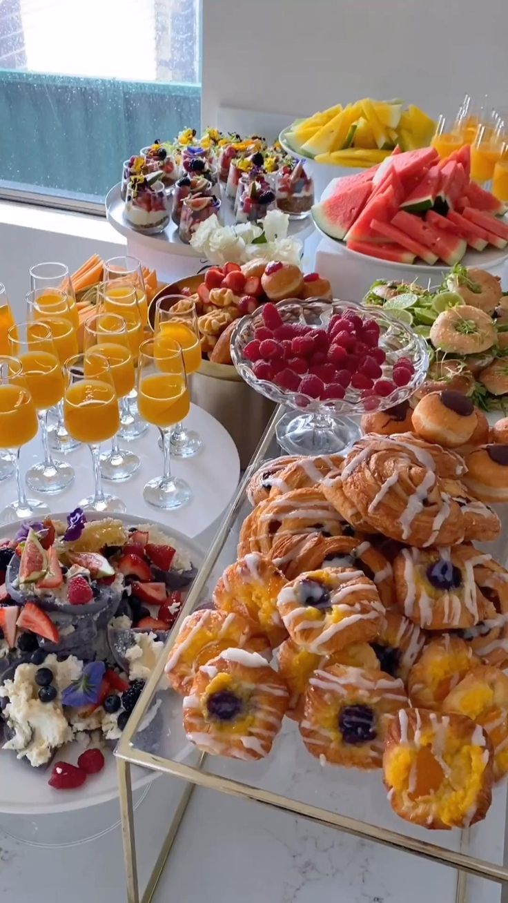 an assortment of pastries and desserts displayed on a buffet table with glasses of orange juice