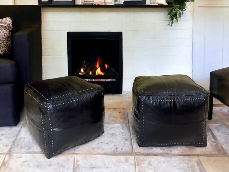 two black leather ottomans sitting in front of a fire place