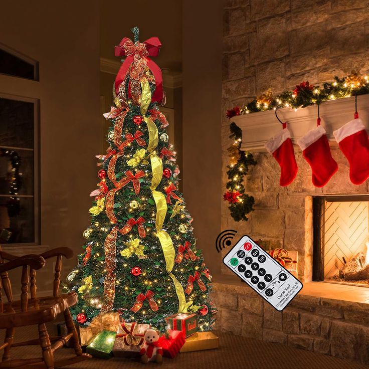 a decorated christmas tree in front of a fireplace with stockings on it and a remote control