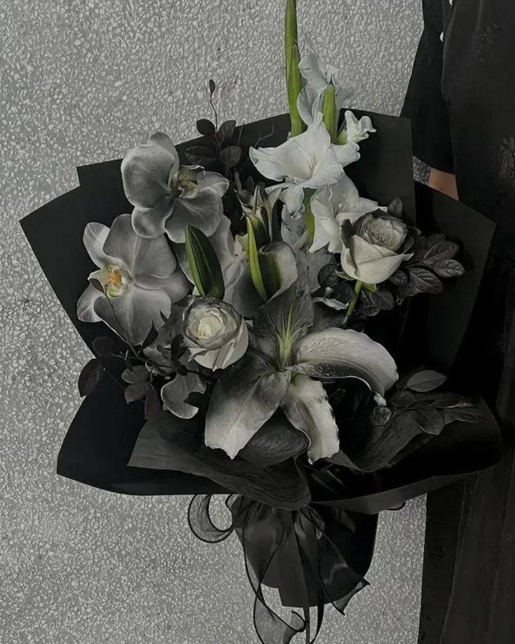 a woman holding a bouquet of white and black flowers in her left hand while standing next to a wall