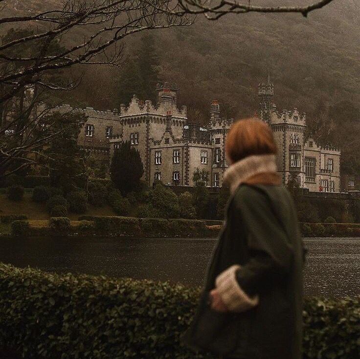 a woman standing in front of a large building on top of a lush green hillside