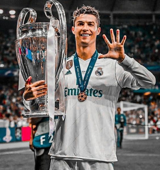 a soccer player holding up a trophy and giving the peace sign with his hand in front of him