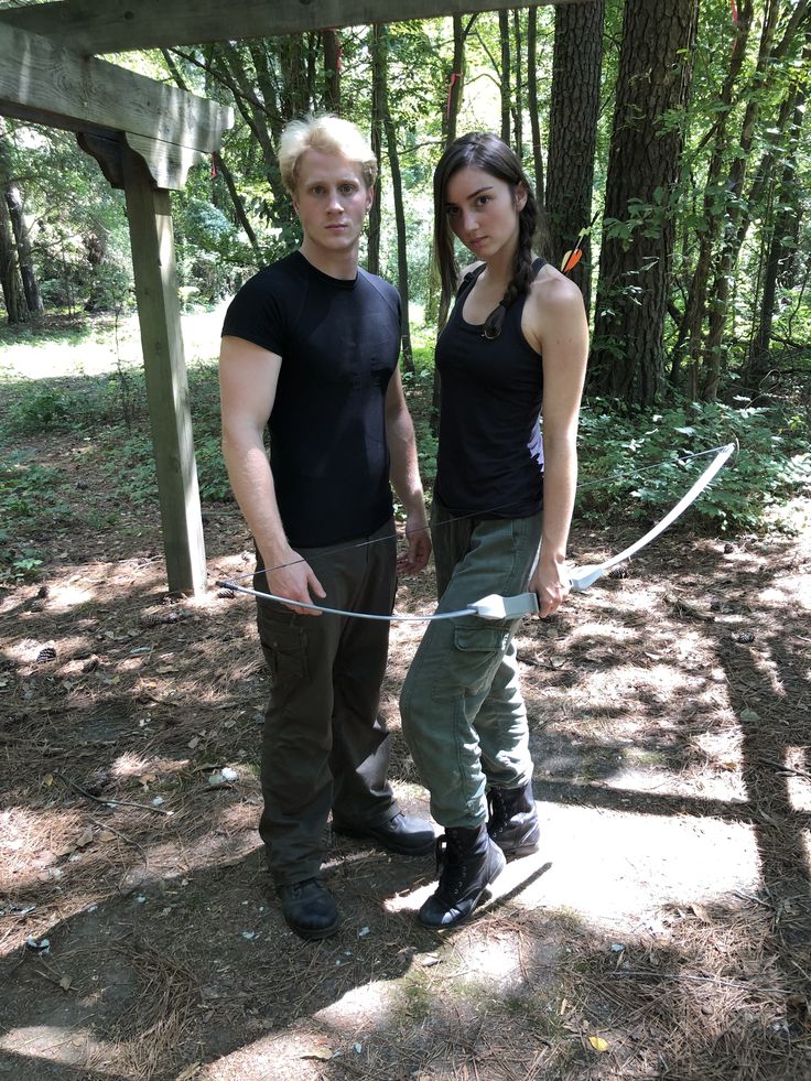 a man and woman standing next to each other in the woods with a rope attached to their backs