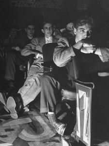 black and white photograph of men sitting in chairs with their feet on each other's legs