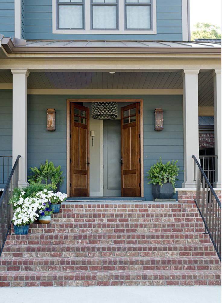 a blue house with two brown doors and some flowers on the front steps in front of it