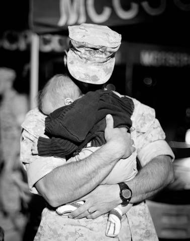 a soldier holding a baby in his arms while wearing a medical mask on top of his head