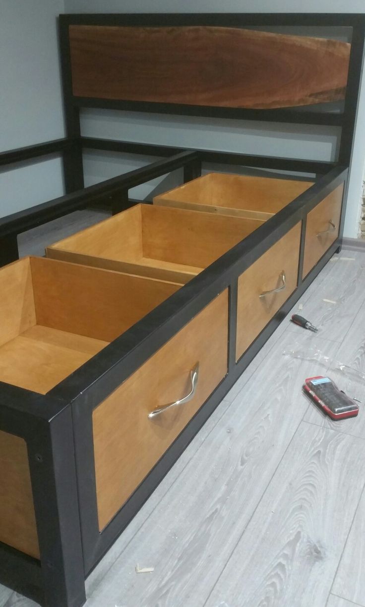 a bed frame with drawers on each side and a cell phone laying on the floor next to it