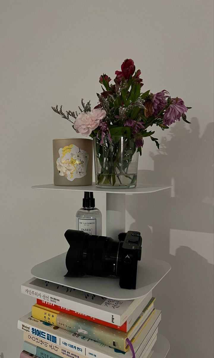 a stack of books with flowers in a glass vase on top and camera next to it