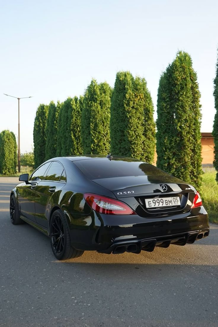 a black mercedes cla parked on the street in front of some tall green trees