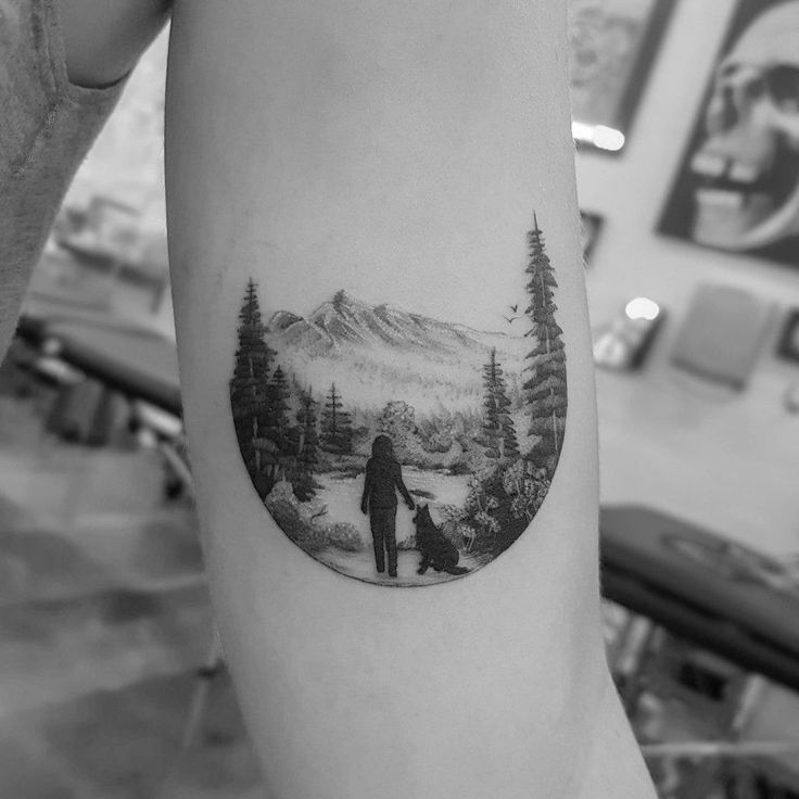 a man and his dog are standing in front of a mountain landscape tattoo on the arm