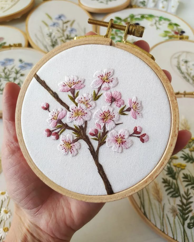 a hand is holding a small embroideryed cherry blossom on a white background with gold trim