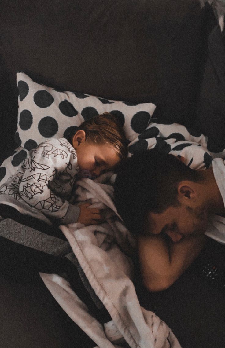 a man and woman laying on top of each other under a polka dot blanket in bed