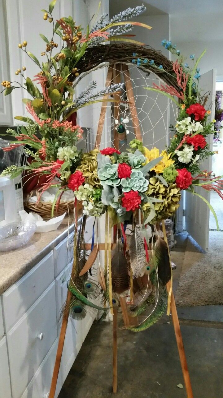 an arrangement of flowers and plants in a basket on a stand next to a kitchen counter