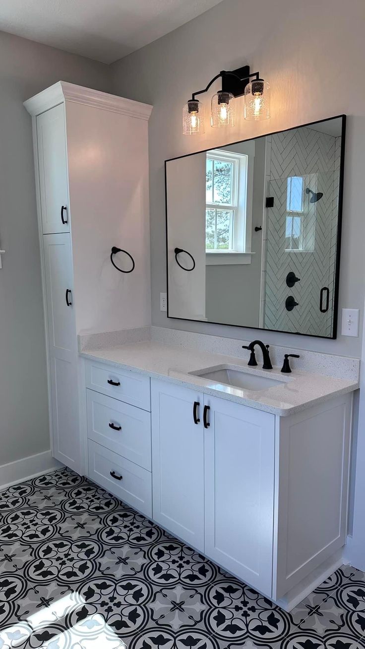 a bathroom with black and white tile flooring next to a large mirror on the wall