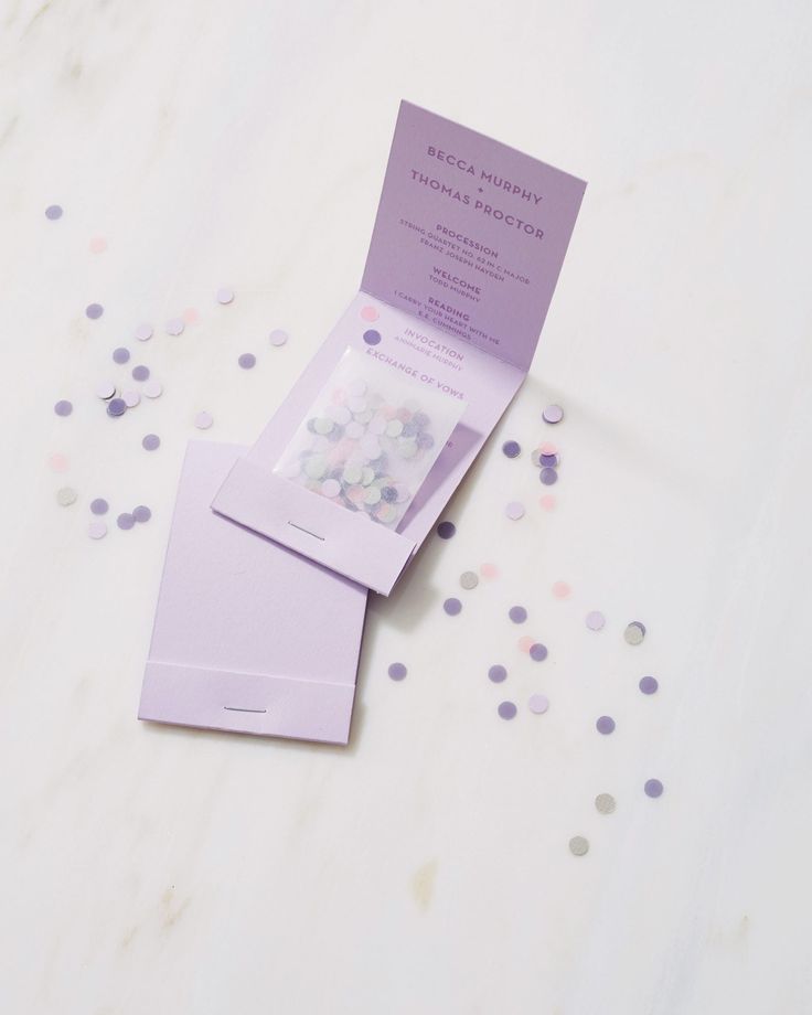 two purple envelopes with confetti scattered around them on a white tablecloth