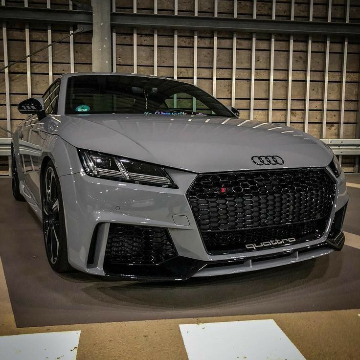 the front end of a grey sports car parked in a parking lot next to a building