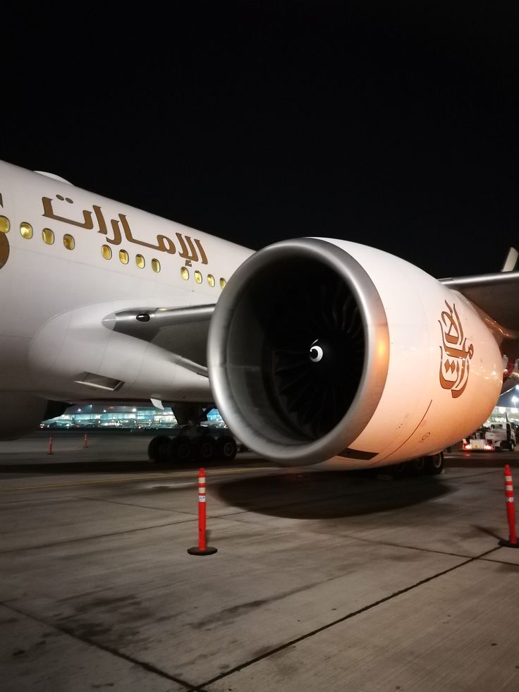 a large jetliner sitting on top of an airport tarmac at night with its lights on