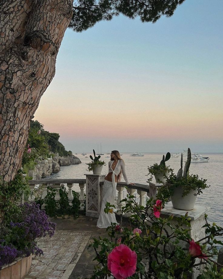 a bride and groom standing on a balcony overlooking the ocean at sunset with pink flowers