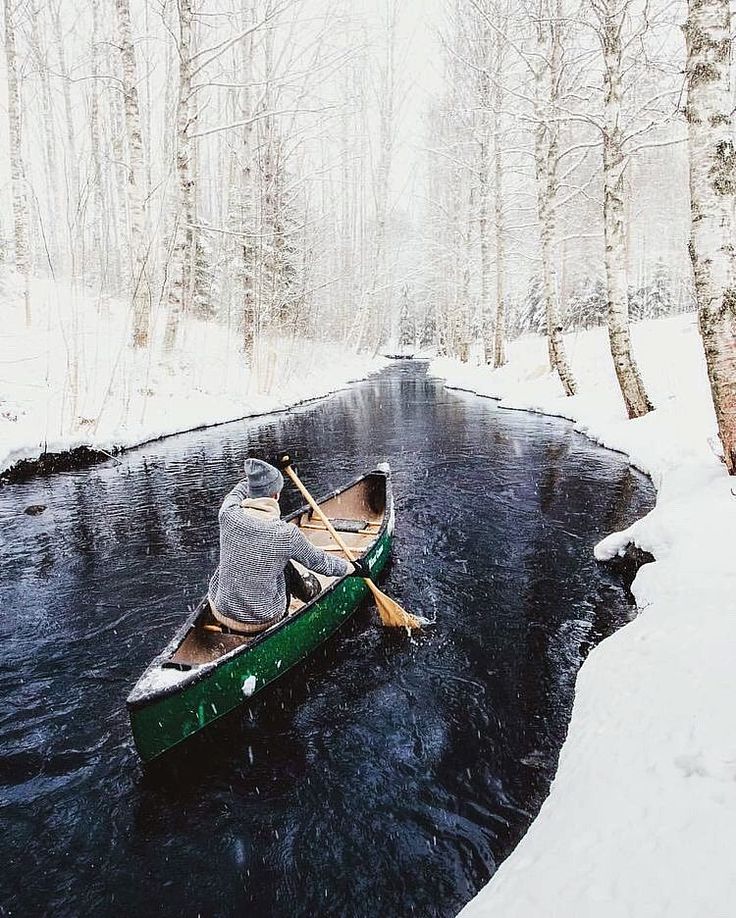 a person in a green canoe paddling down a river with snow on the ground