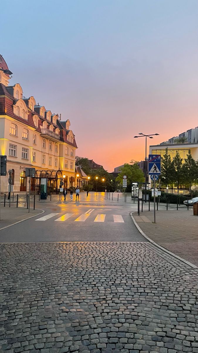 a cobblestone street with buildings and people walking on it at sunset or dawn