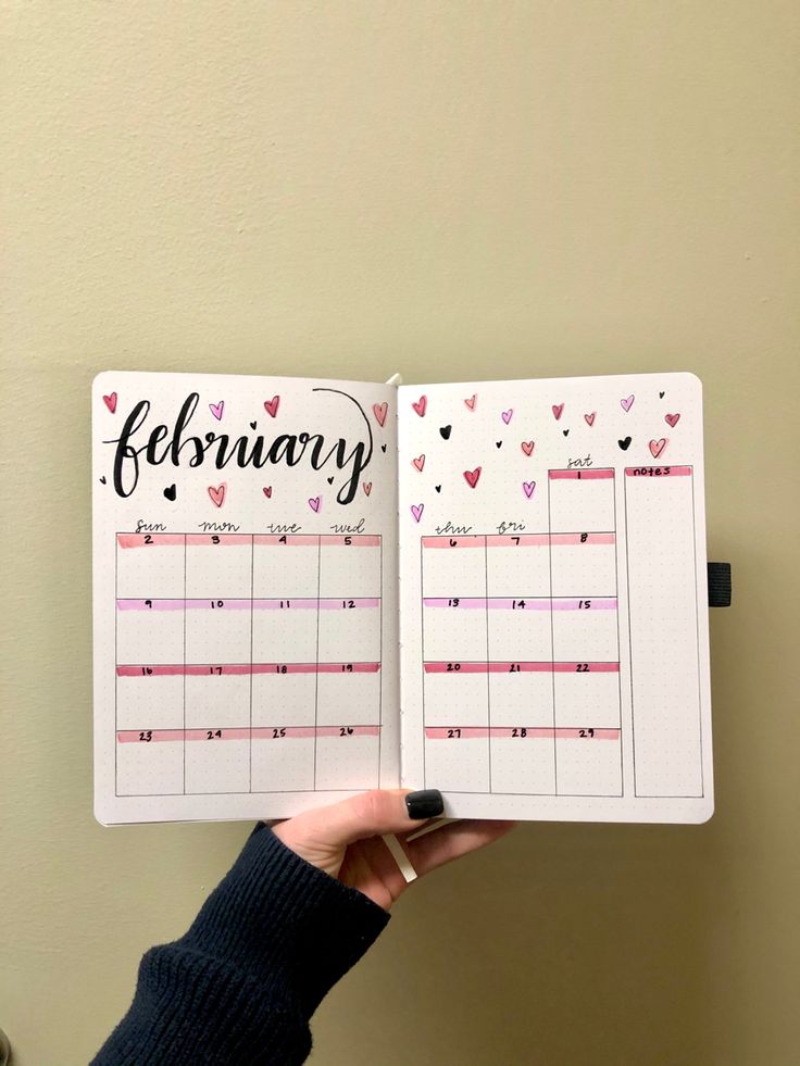 a person holding up a planner with hearts on the pages and writing in black ink