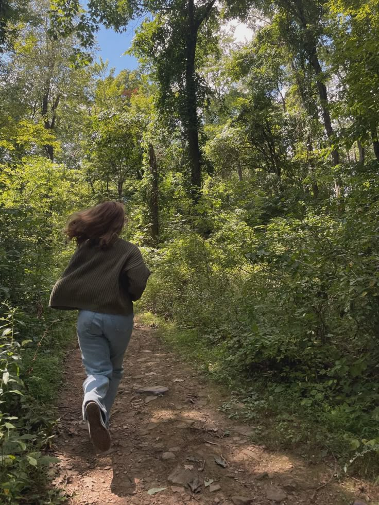 a woman walking down a dirt path in the woods