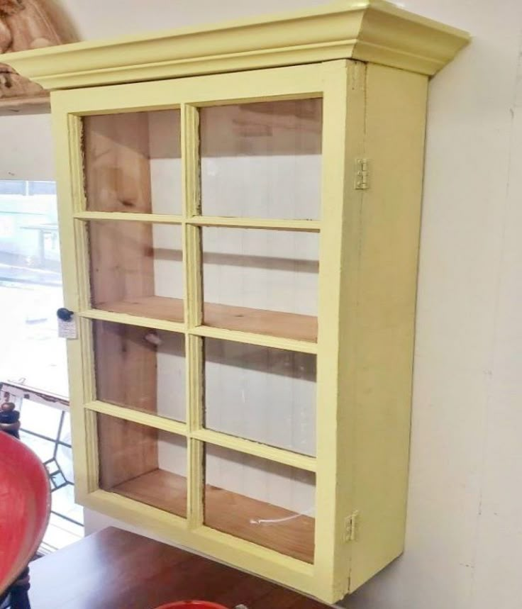 a yellow china cabinet sitting on top of a wooden floor next to a red vase