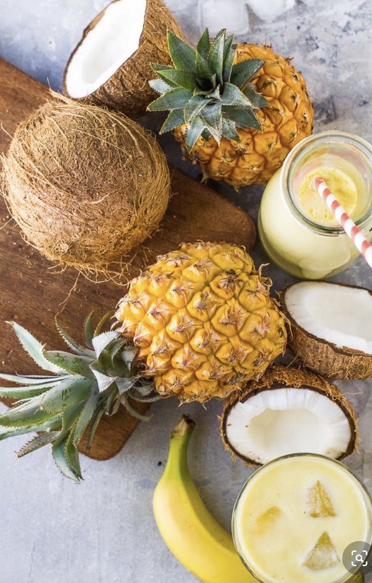 two pineapples and one banana on a cutting board next to some other fruit