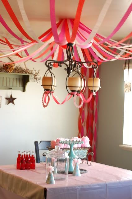 the table is set up for a party with pink and red streamers hanging from the ceiling