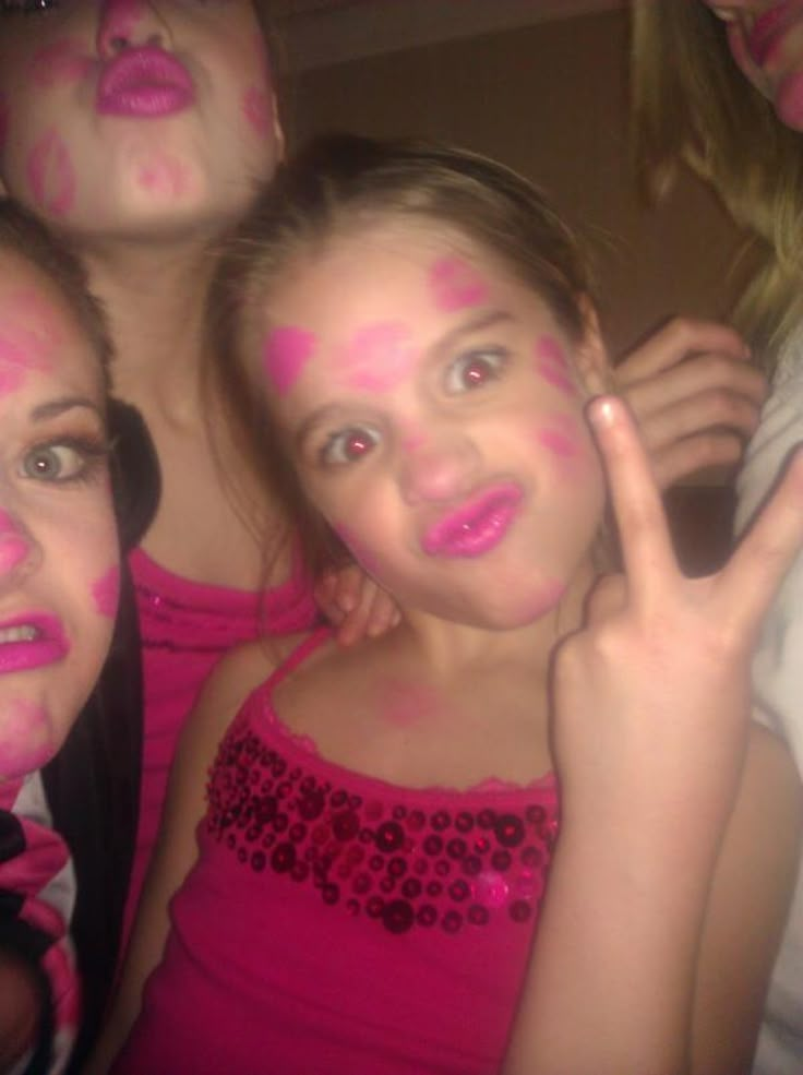 three girls with their faces painted pink and holding up the peace sign in front of them