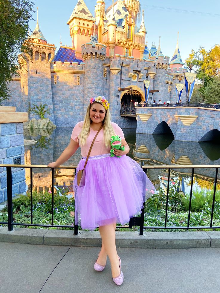 a woman standing in front of a castle wearing a purple tutu skirt and pink shoes