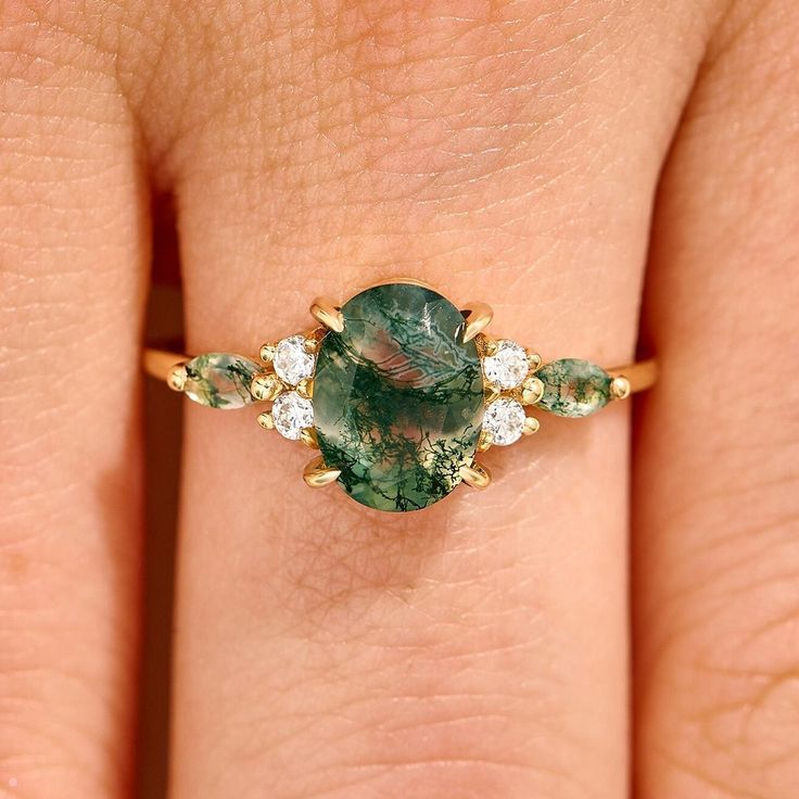 a woman's hand holding a green and white ring with three diamonds on it