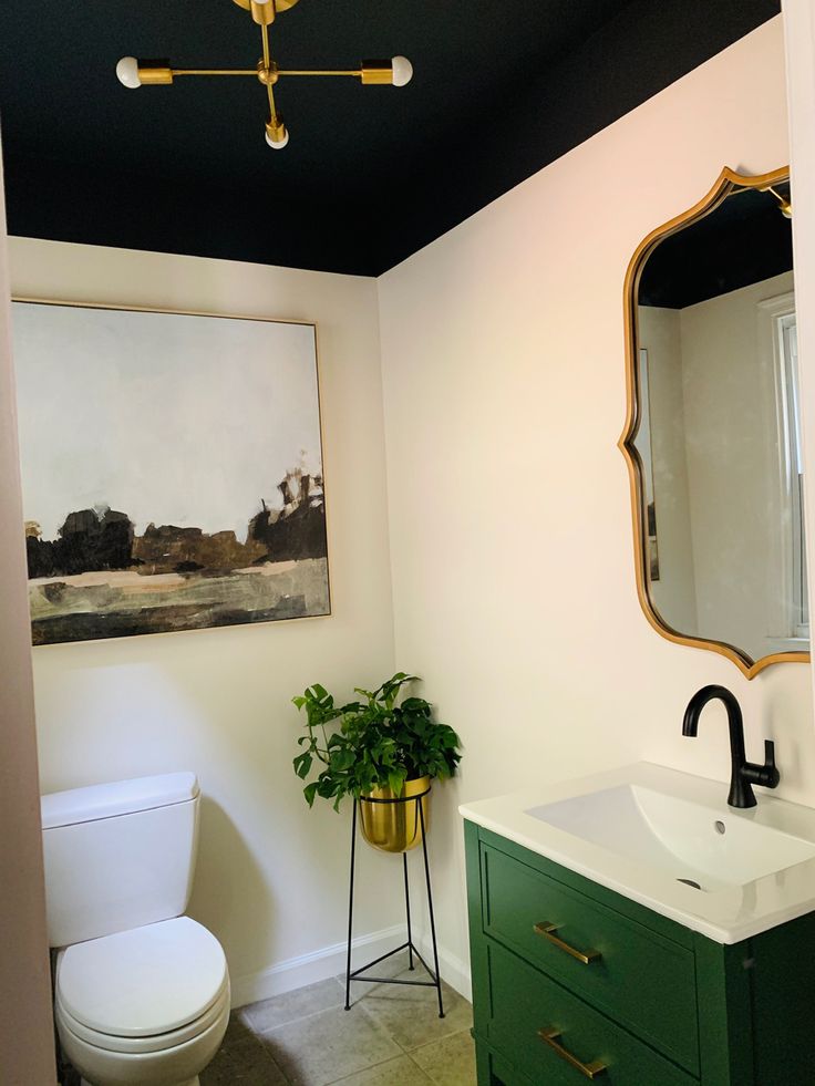 a white toilet sitting next to a green cabinet in a bathroom under a painting on the wall