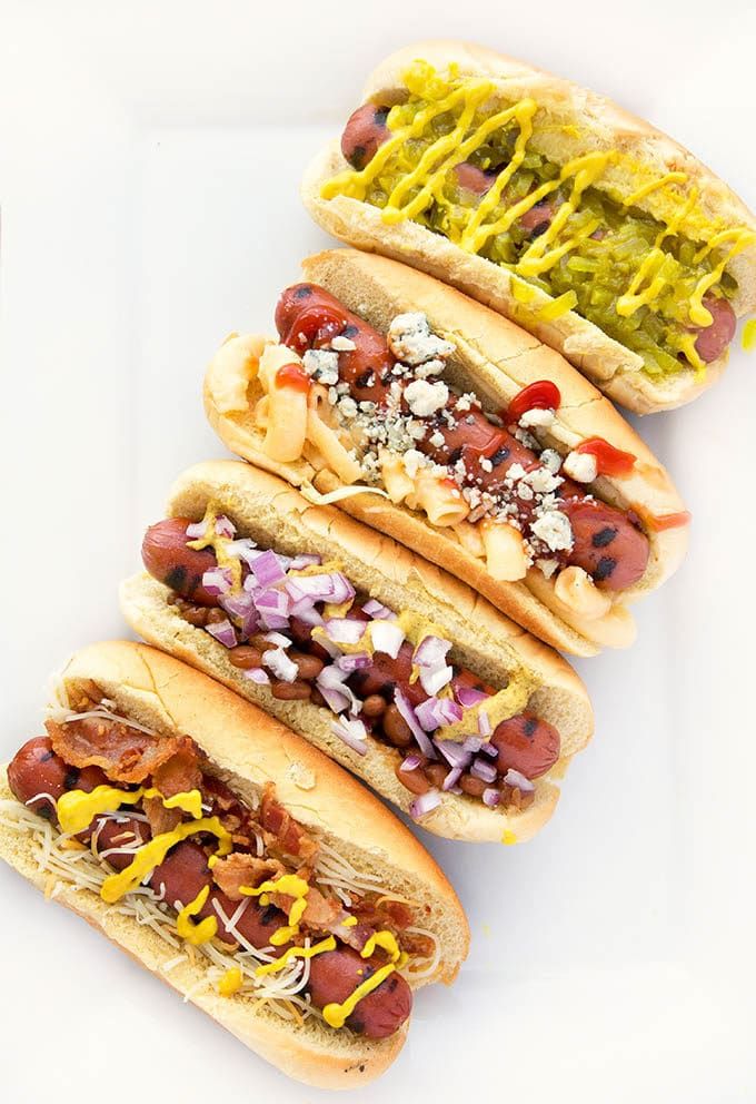 four hot dogs with condiments on them are lined up