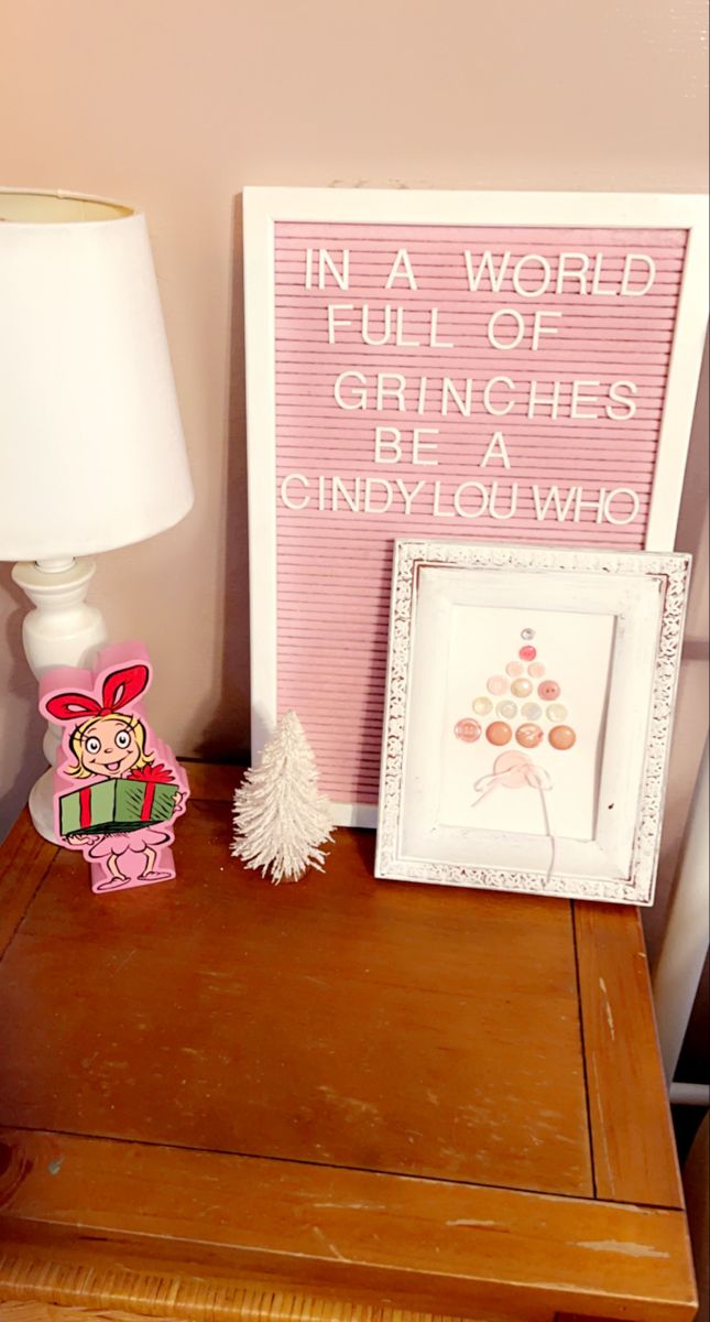 a wooden table with a lamp and some pictures on top of it in front of a pink wall