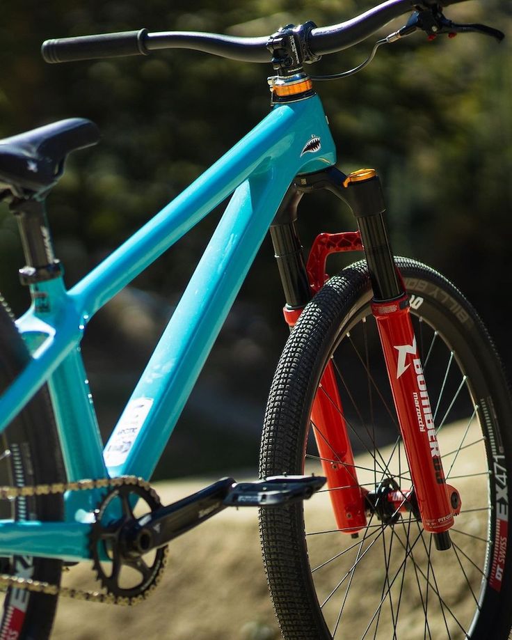 a blue and red mountain bike parked on the side of a road with trees in the background